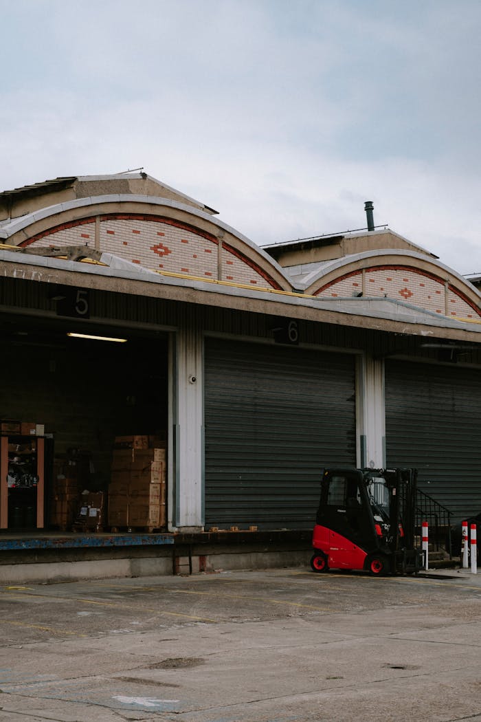 A red forklift parked at a warehouse loading dock with closed garage doors.